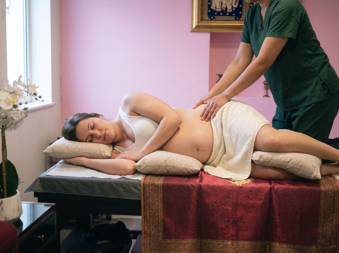 A pregnant client lying on her side, supported by pillows, while a therapist massages her lower back